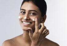 Beautiful and happy woman applying moisturizing cream on her face