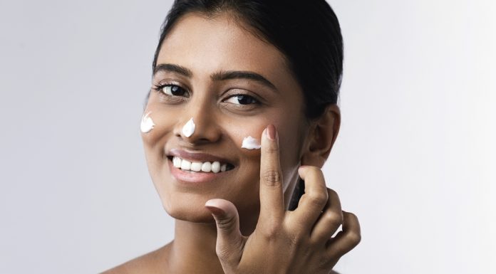 Beautiful and happy woman applying moisturizing cream on her face
