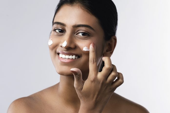 Beautiful and happy woman applying moisturizing cream on her face